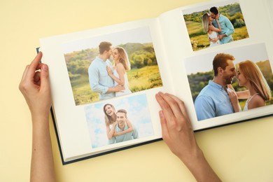 Woman looking at family photos in photo album on beige background, top view