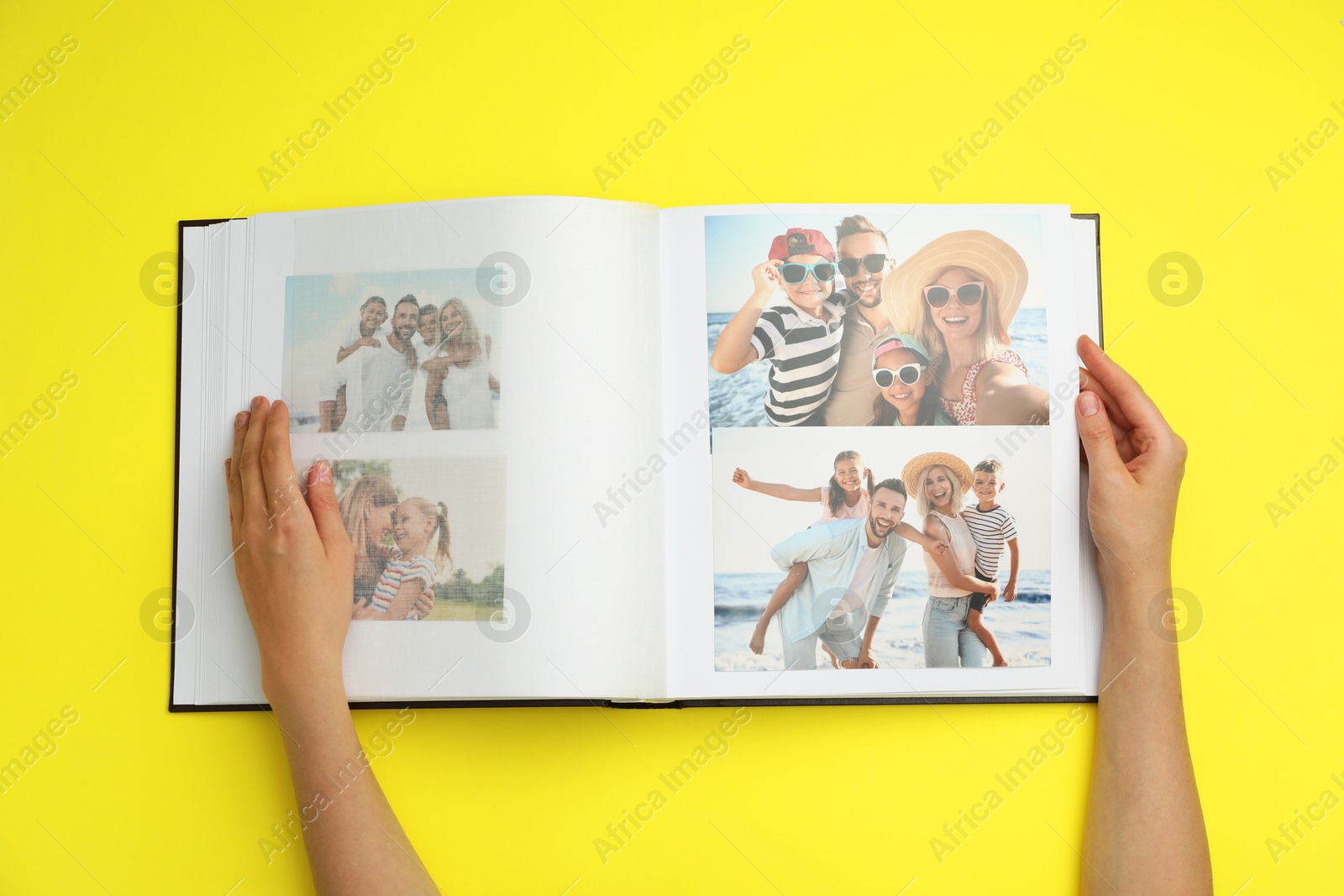 Photo of Woman looking at family photos in photo album on yellow background, top view