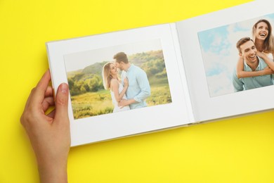 Woman looking at family photos in photo album on yellow background, top view