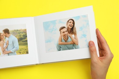 Photo of Woman looking at family photos in photo album on yellow background, top view