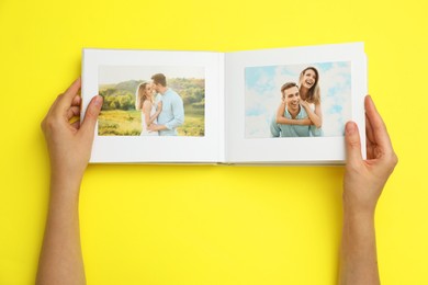 Photo of Woman looking at family photos in photo album on yellow background, top view