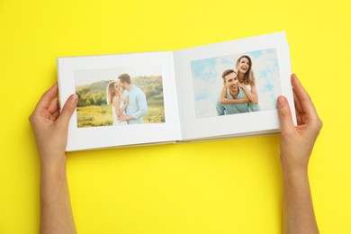 Photo of Woman looking at family photos in photo album on yellow background, top view