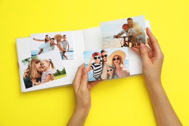 Photo of Woman with open photo album and different photos on yellow background, top view