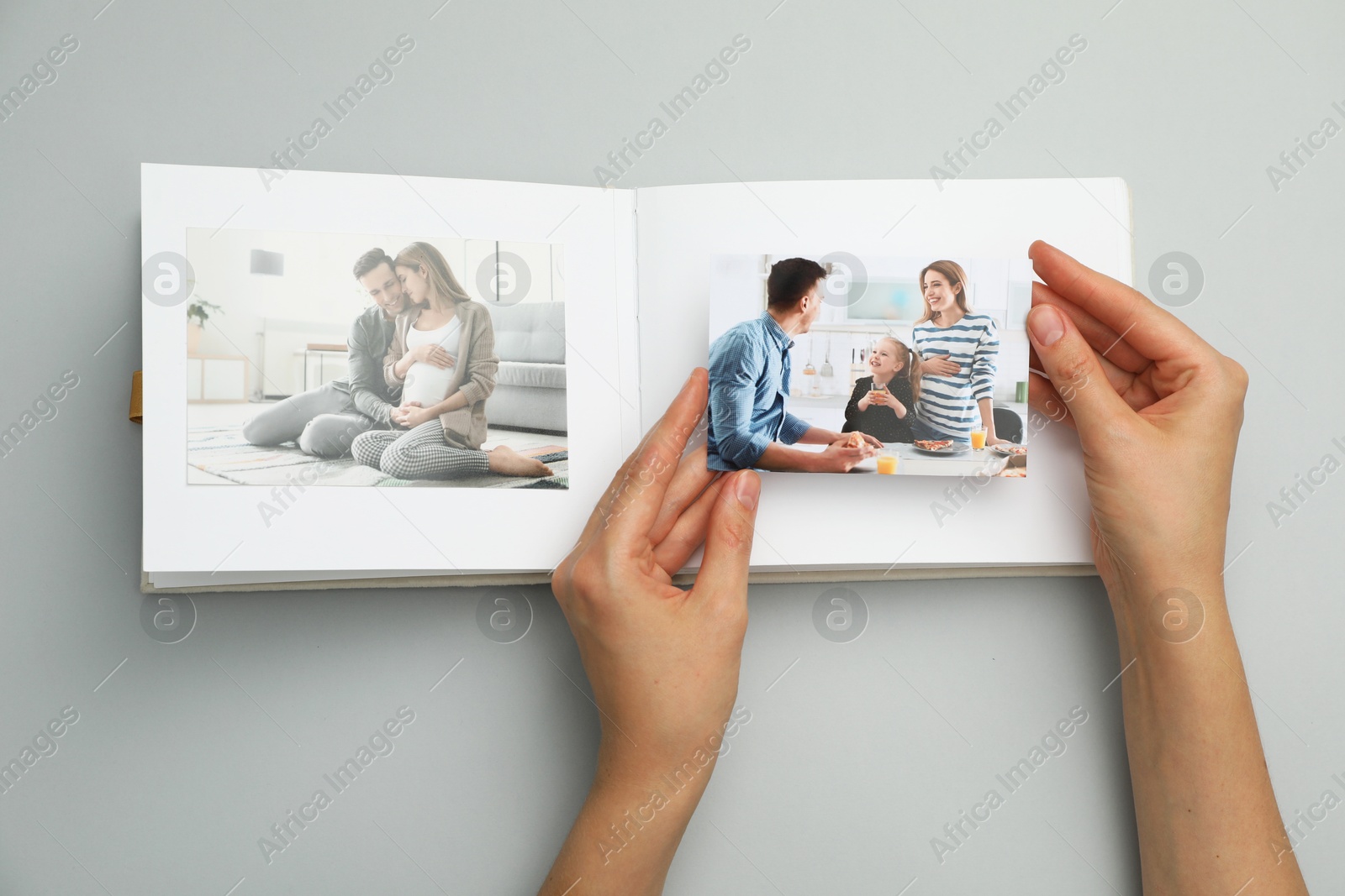 Photo of Woman with open photo album and photos on grey background, top view