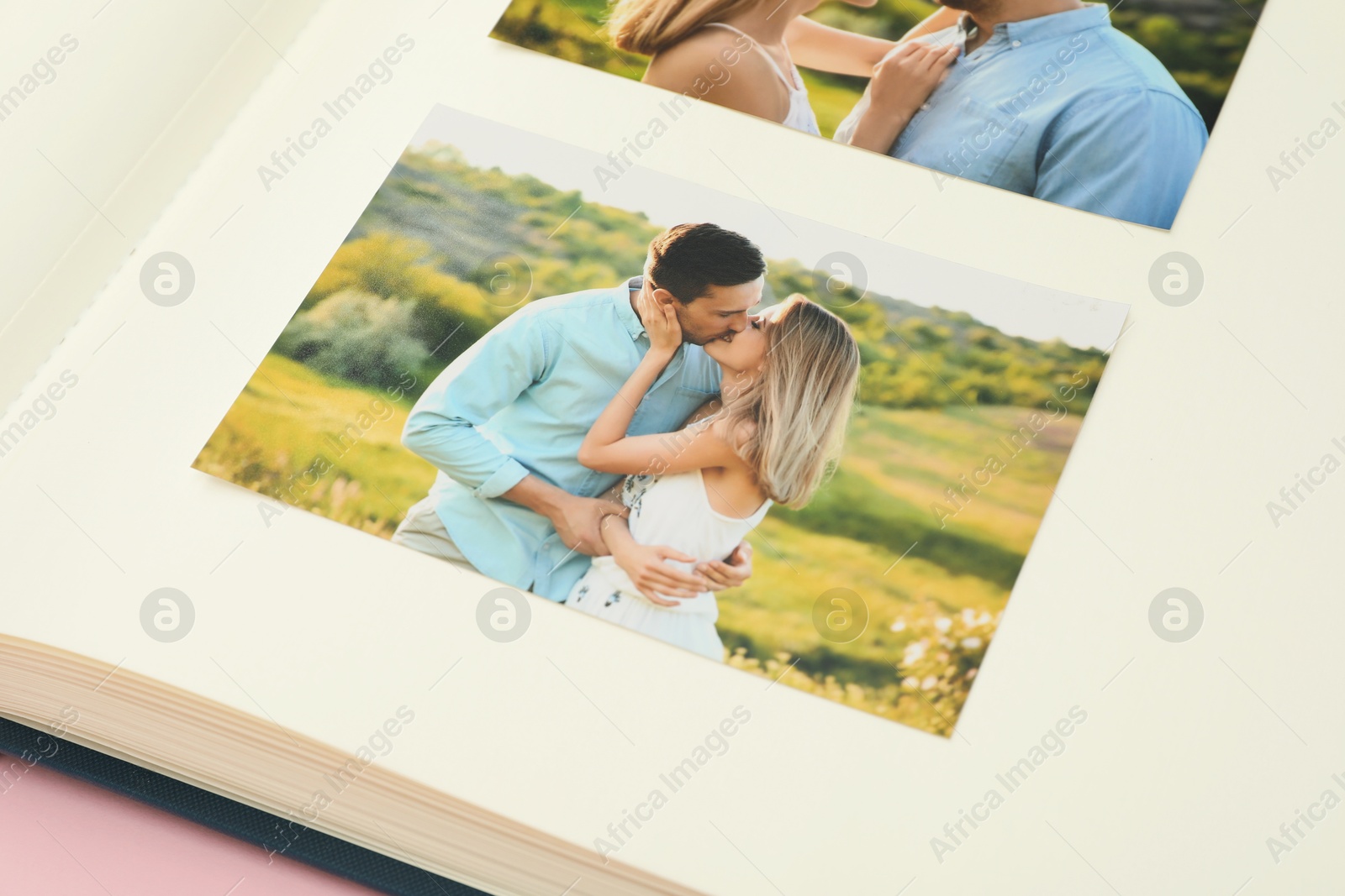 Photo of Open photo album with photos on pink background, closeup