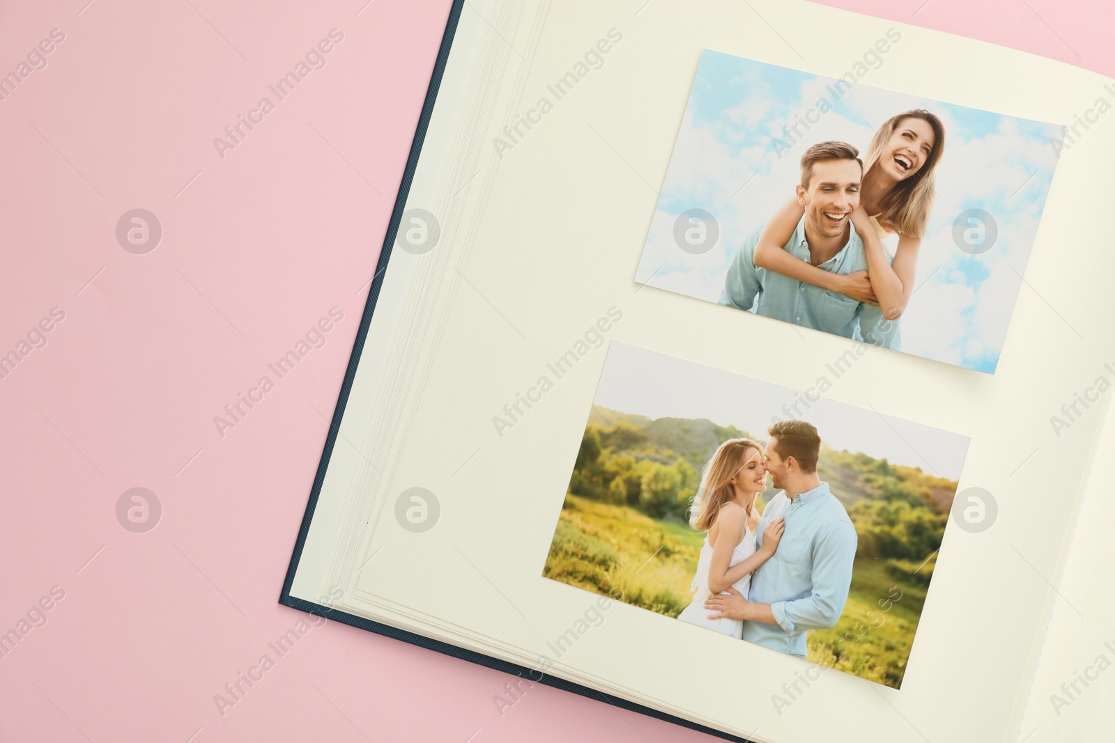 Photo of Open photo album with photos on pink background, top view