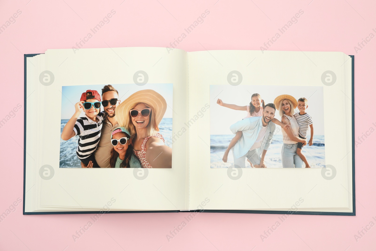 Photo of Open photo album with photos on pink background, top view