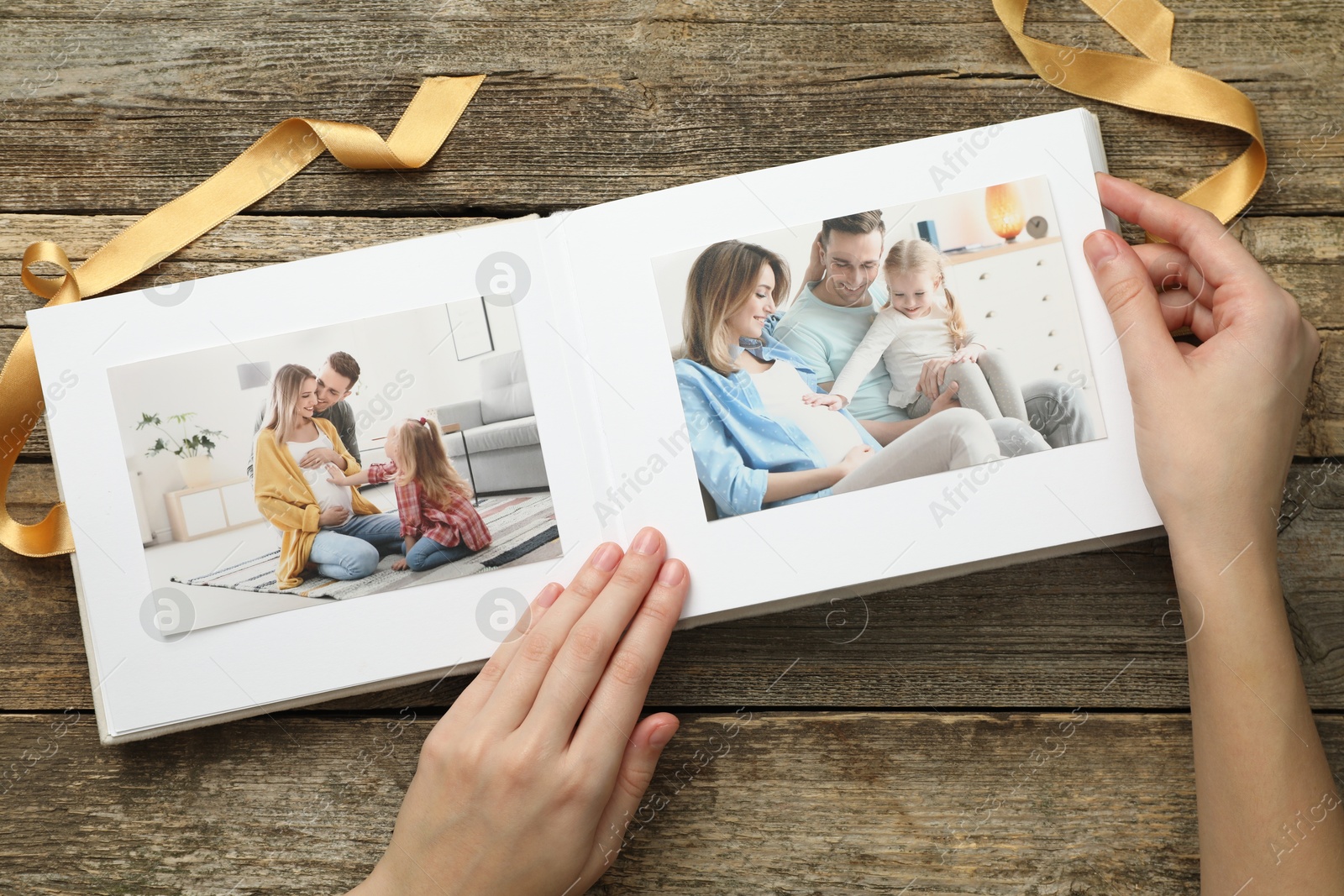 Photo of Woman with different photos in open photo album at wooden table, top view