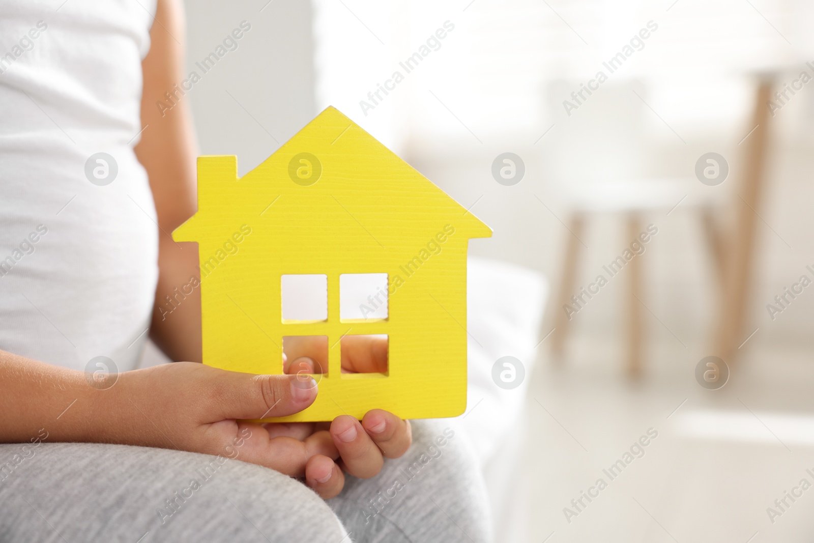 Photo of Orphanage concept. Little girl with yellow house model indoors, closeup. Space for text