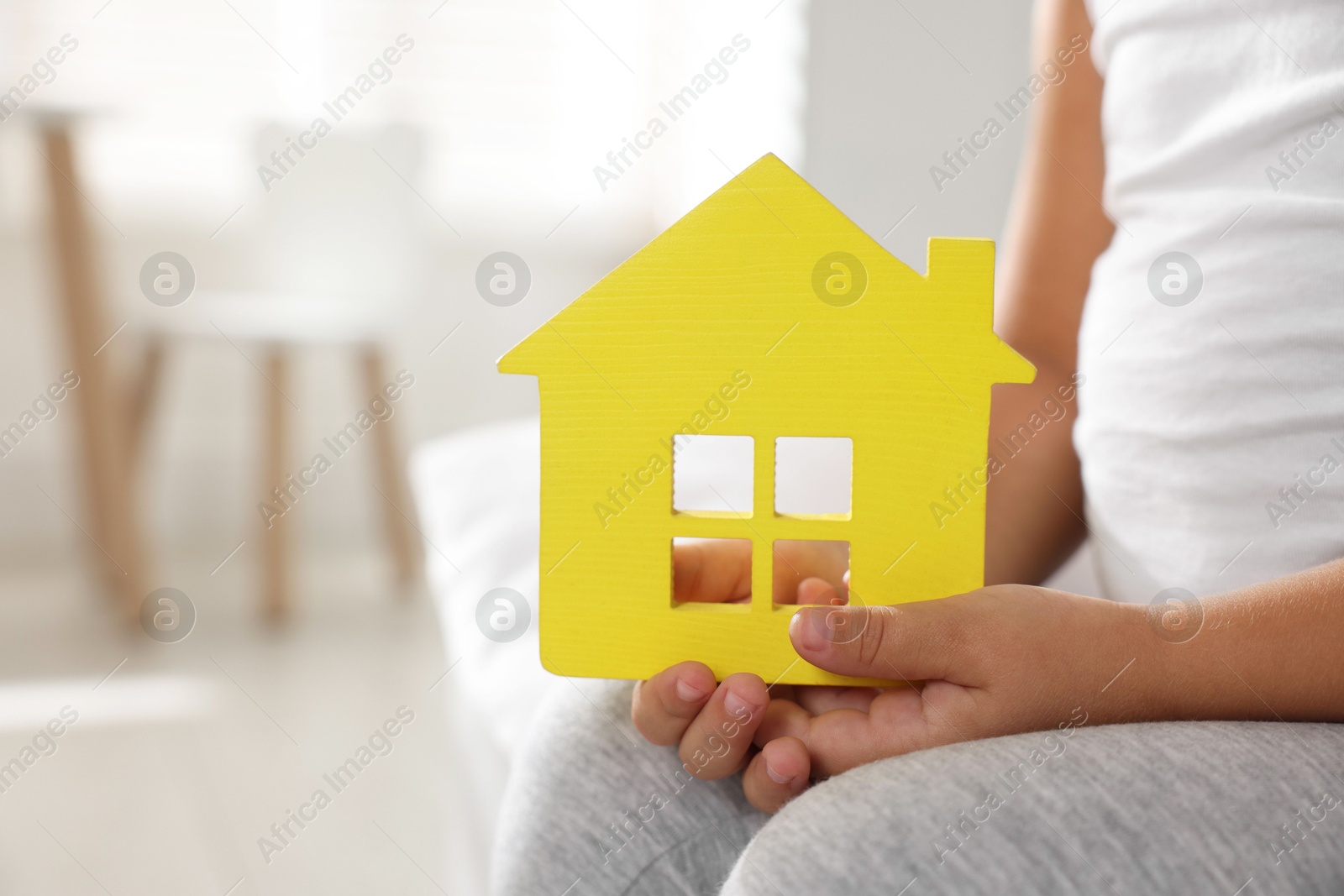 Photo of Orphanage concept. Little girl with yellow house model indoors, closeup. Space for text