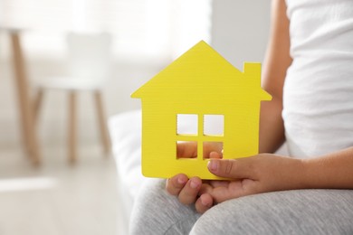 Photo of Orphanage concept. Little girl with yellow house model indoors, closeup. Space for text