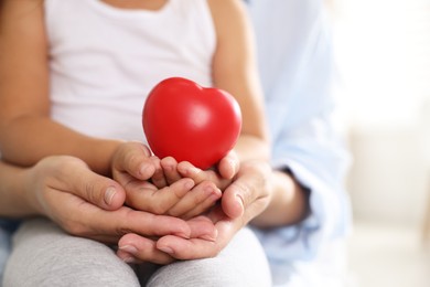 Photo of Little girl and her mother with red heart figure indoors, closeup