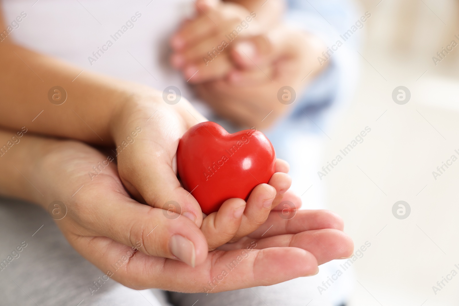 Photo of Little girl and her mother with red heart figure indoors, closeup