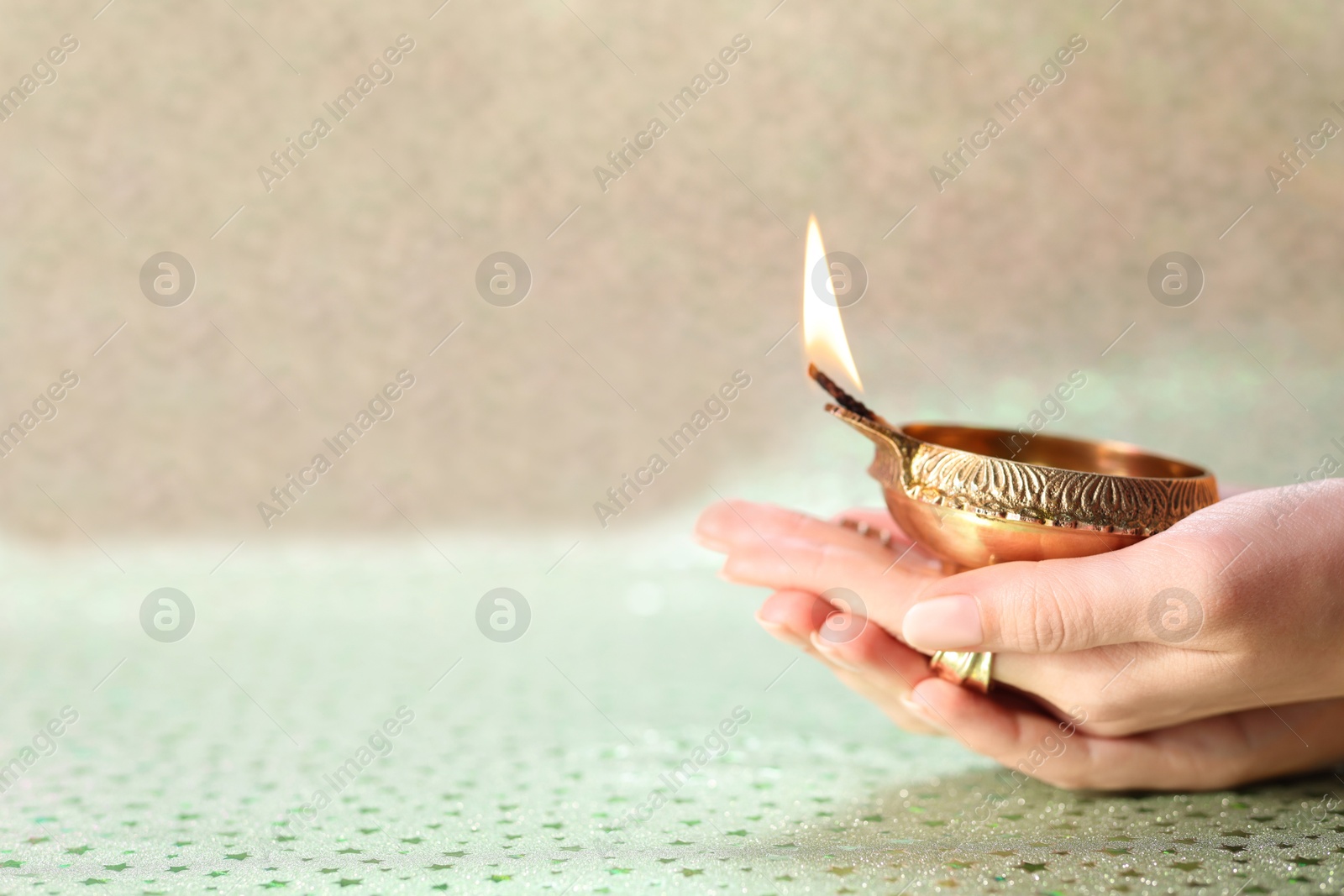 Photo of Diwali celebration. Woman holding lit diya lamp on color background, closeup. Space for text