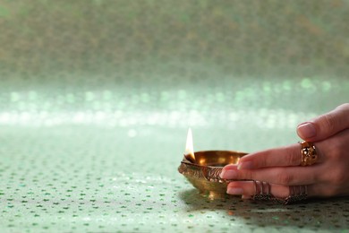 Photo of Diwali celebration. Woman with lit diya lamp on color background, closeup. Space for text