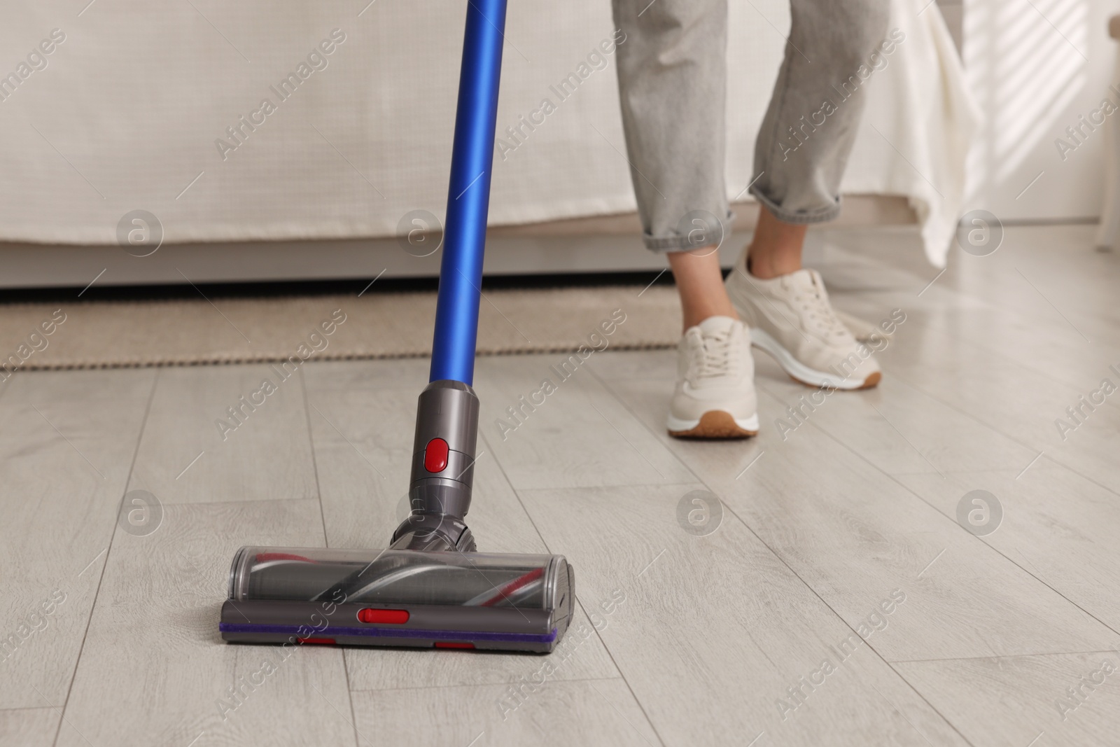 Photo of Woman cleaning floor with cordless vacuum cleaner indoors, closeup