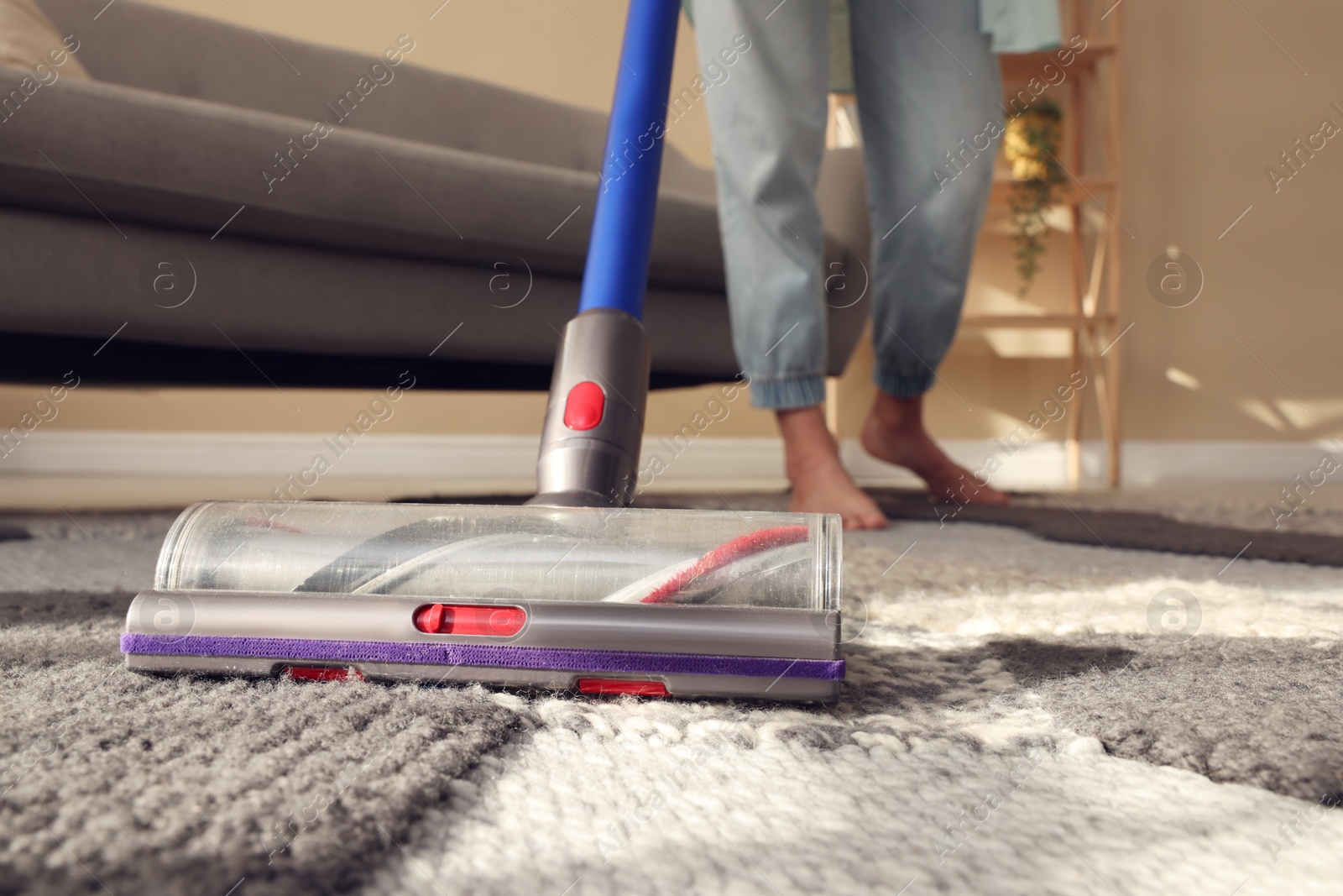 Photo of Woman cleaning rug with cordless vacuum cleaner at home, closeup