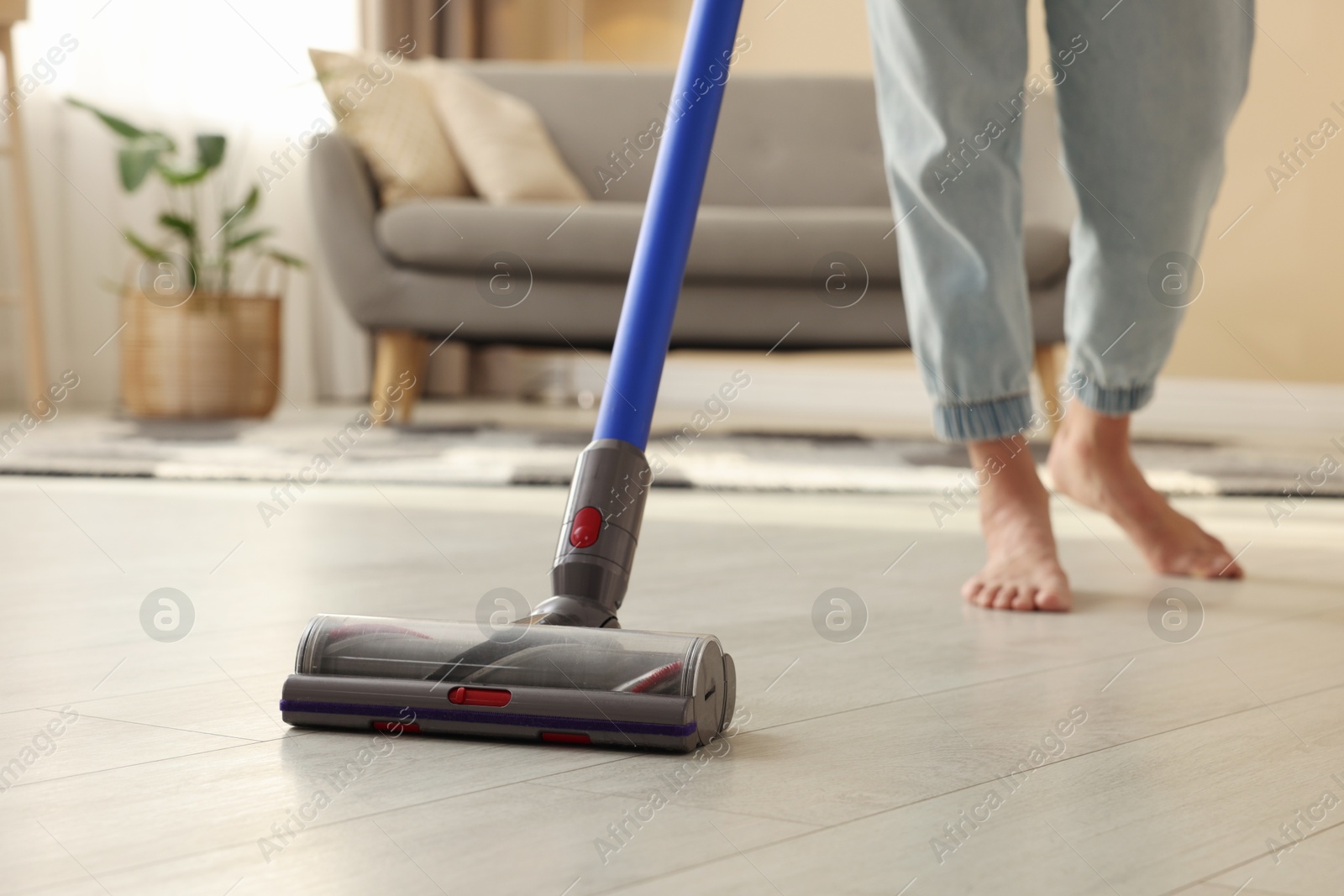 Photo of Woman cleaning floor with cordless vacuum cleaner at home, closeup