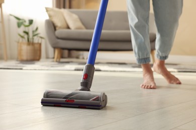 Photo of Woman cleaning floor with cordless vacuum cleaner at home, closeup