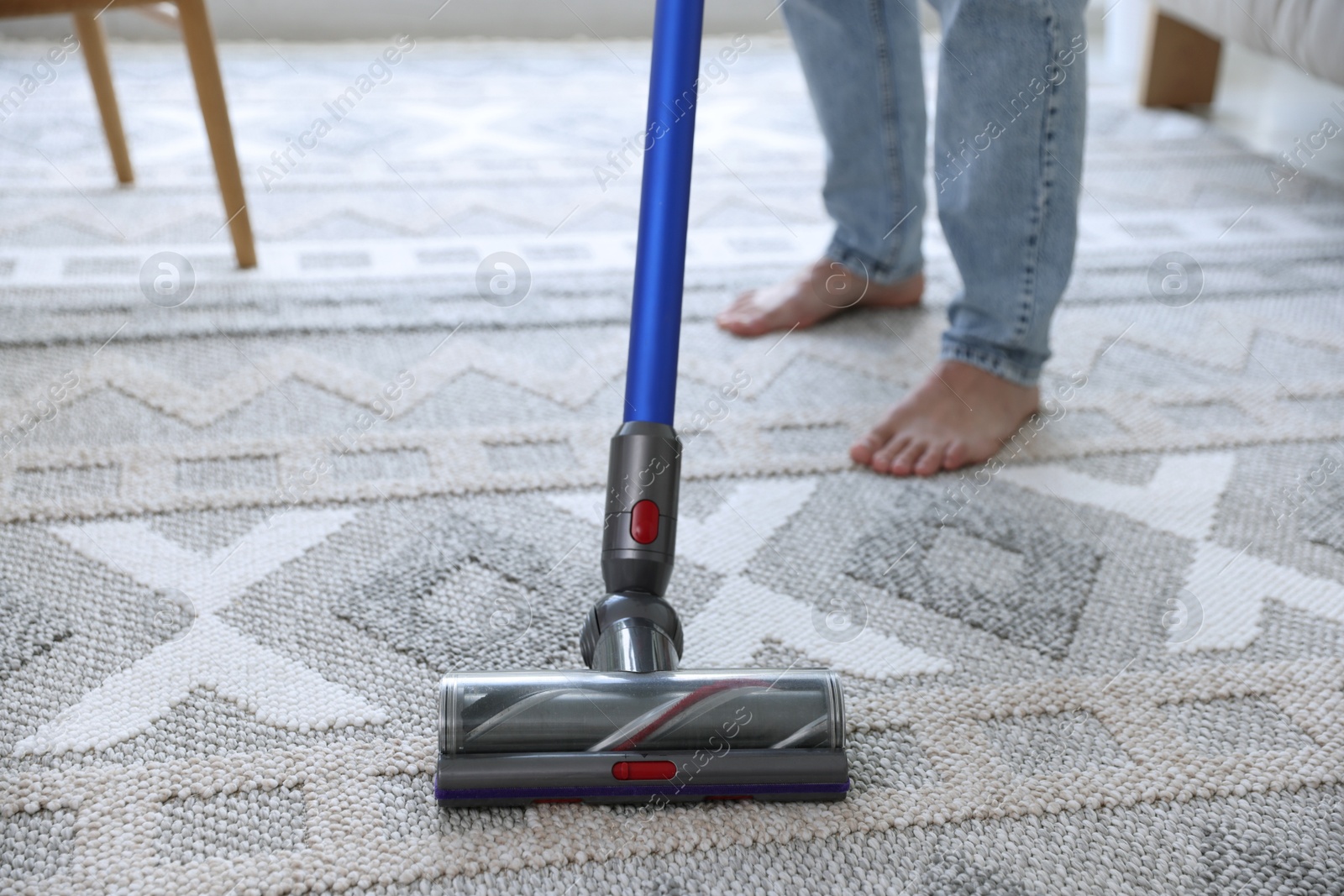 Photo of Man cleaning rug with cordless vacuum cleaner at home, closeup