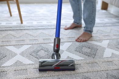 Photo of Man cleaning rug with cordless vacuum cleaner at home, closeup