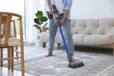 Photo of Man cleaning rug with cordless vacuum cleaner at home, closeup