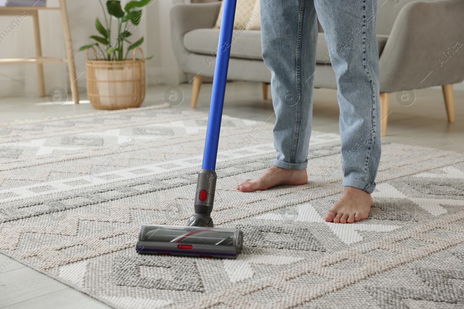 Photo of Man cleaning rug with cordless vacuum cleaner at home, closeup