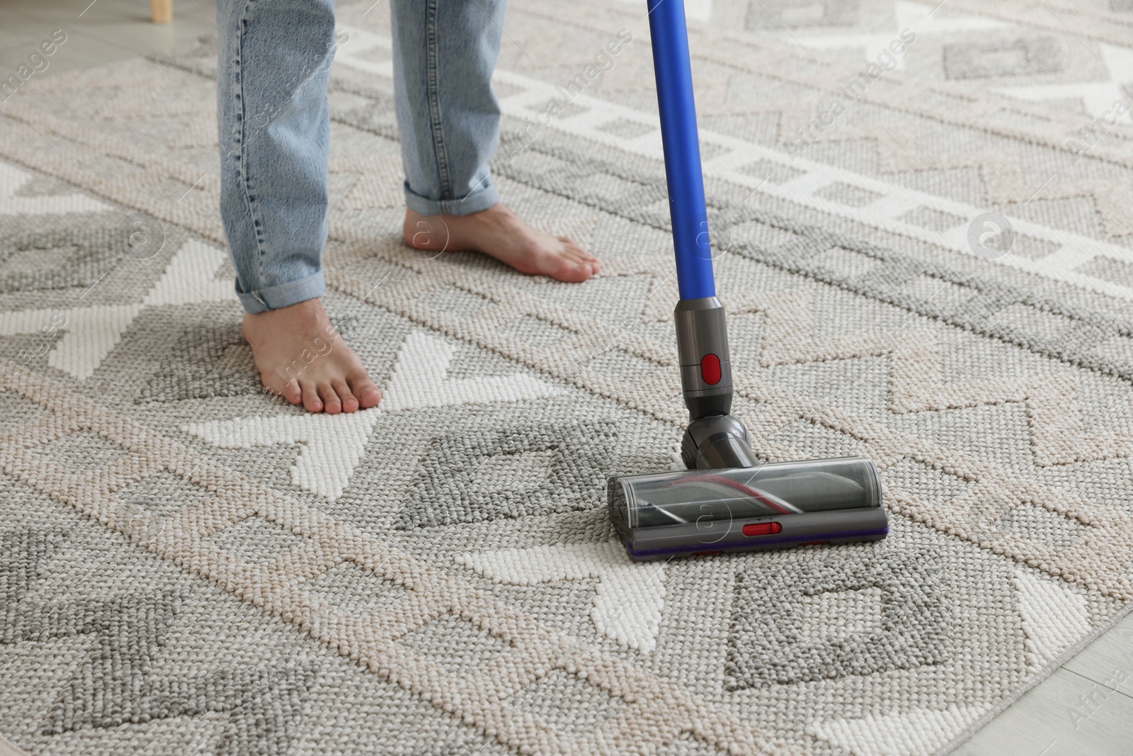 Photo of Man cleaning rug with cordless vacuum cleaner at home, closeup