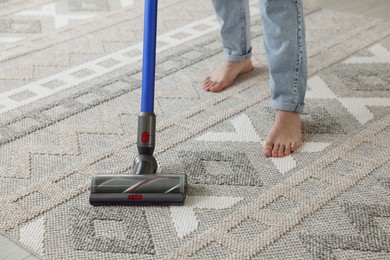 Photo of Man cleaning rug with cordless vacuum cleaner at home, closeup