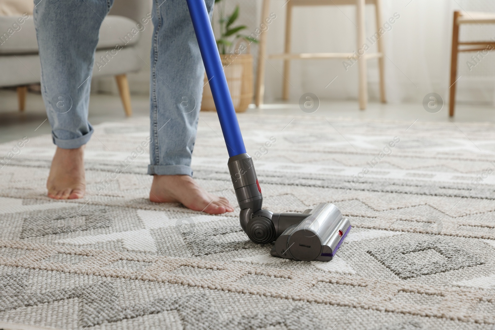 Photo of Man cleaning rug with cordless vacuum cleaner at home, closeup