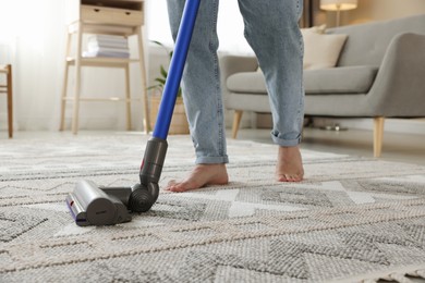 Photo of Man cleaning rug with cordless vacuum cleaner at home, closeup