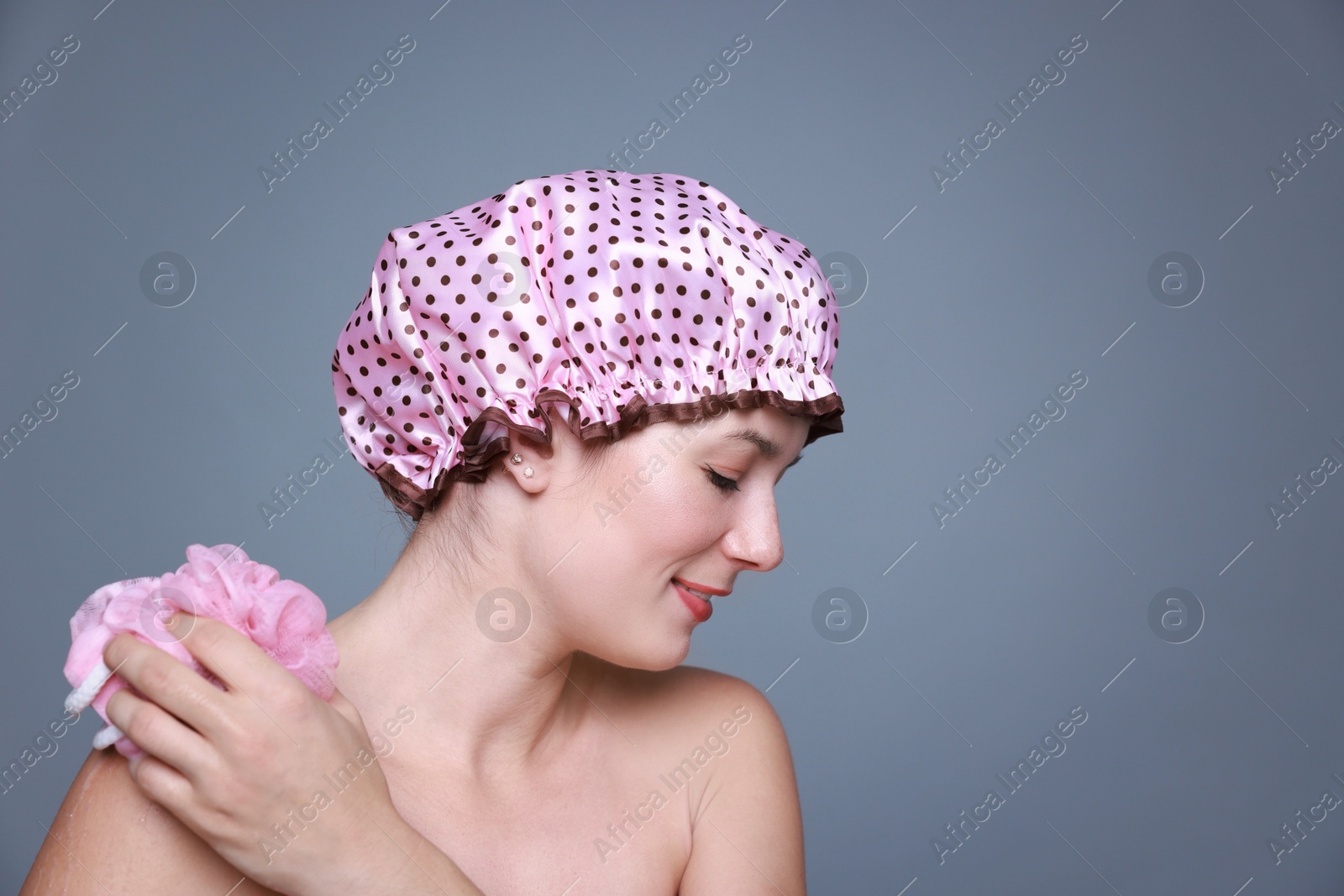 Photo of Woman with shower cap and mesh sponge on grey background, space for text