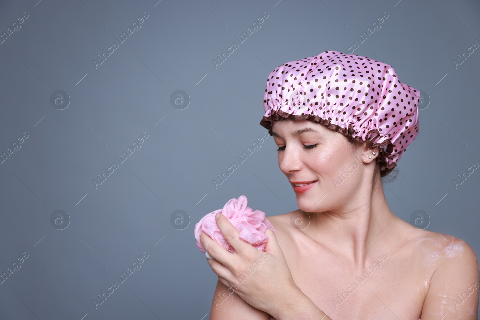 Photo of Woman with shower cap and mesh sponge on grey background, space for text