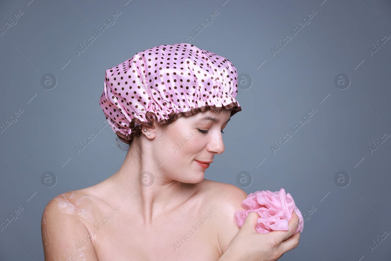 Photo of Woman with shower cap and mesh sponge on grey background