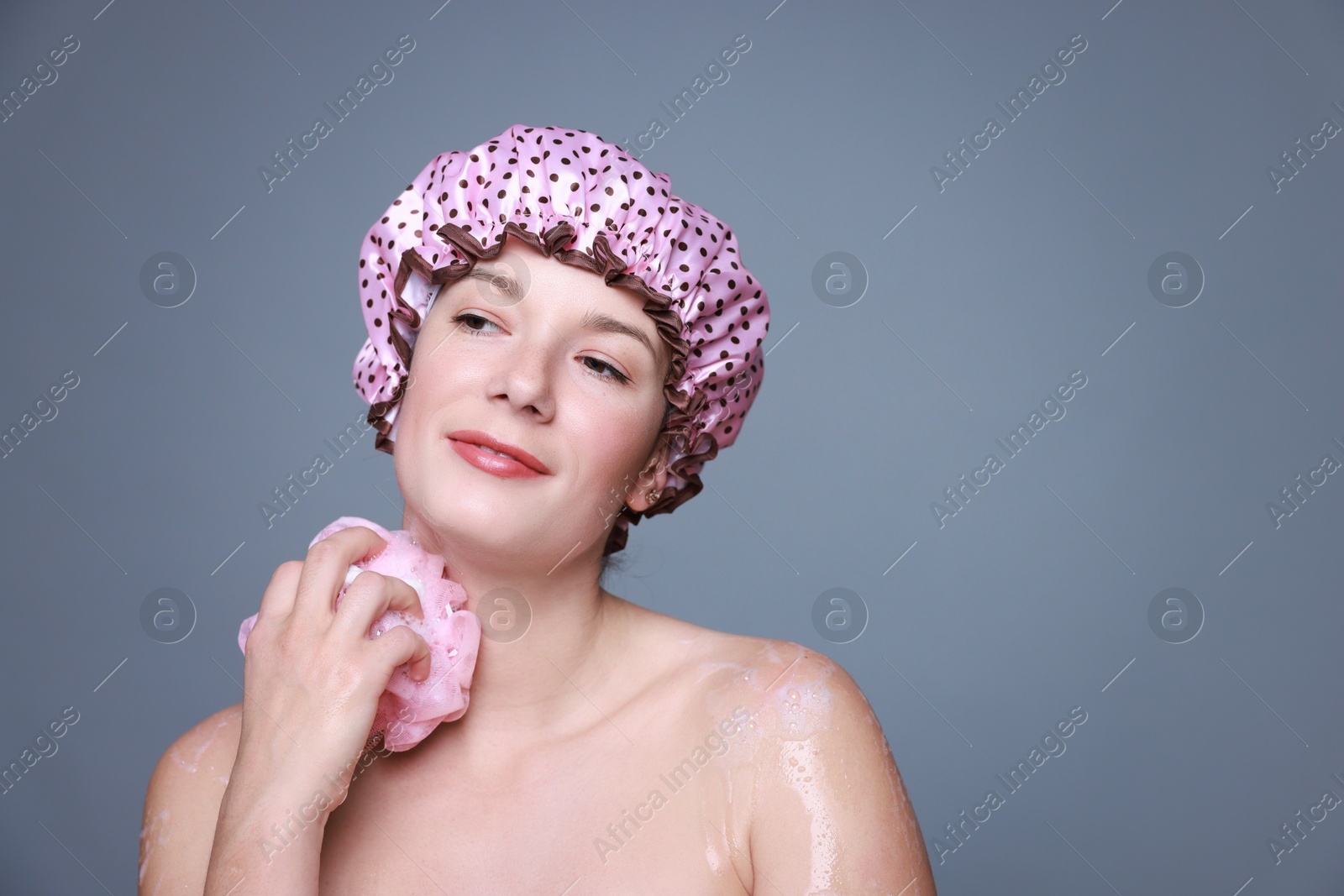 Photo of Woman with shower cap and mesh sponge on grey background, space for text