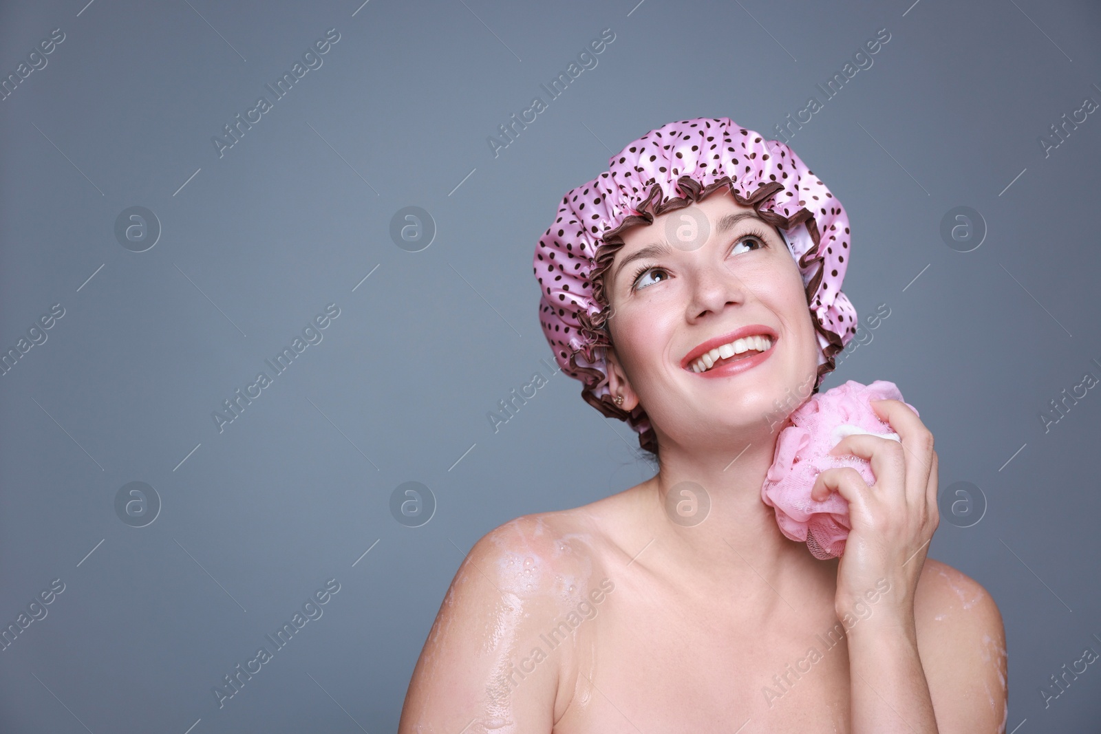 Photo of Woman with shower cap and mesh sponge on grey background, space for text