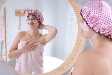 Photo of Woman with shower cap and cream on her face near mirror in bathroom