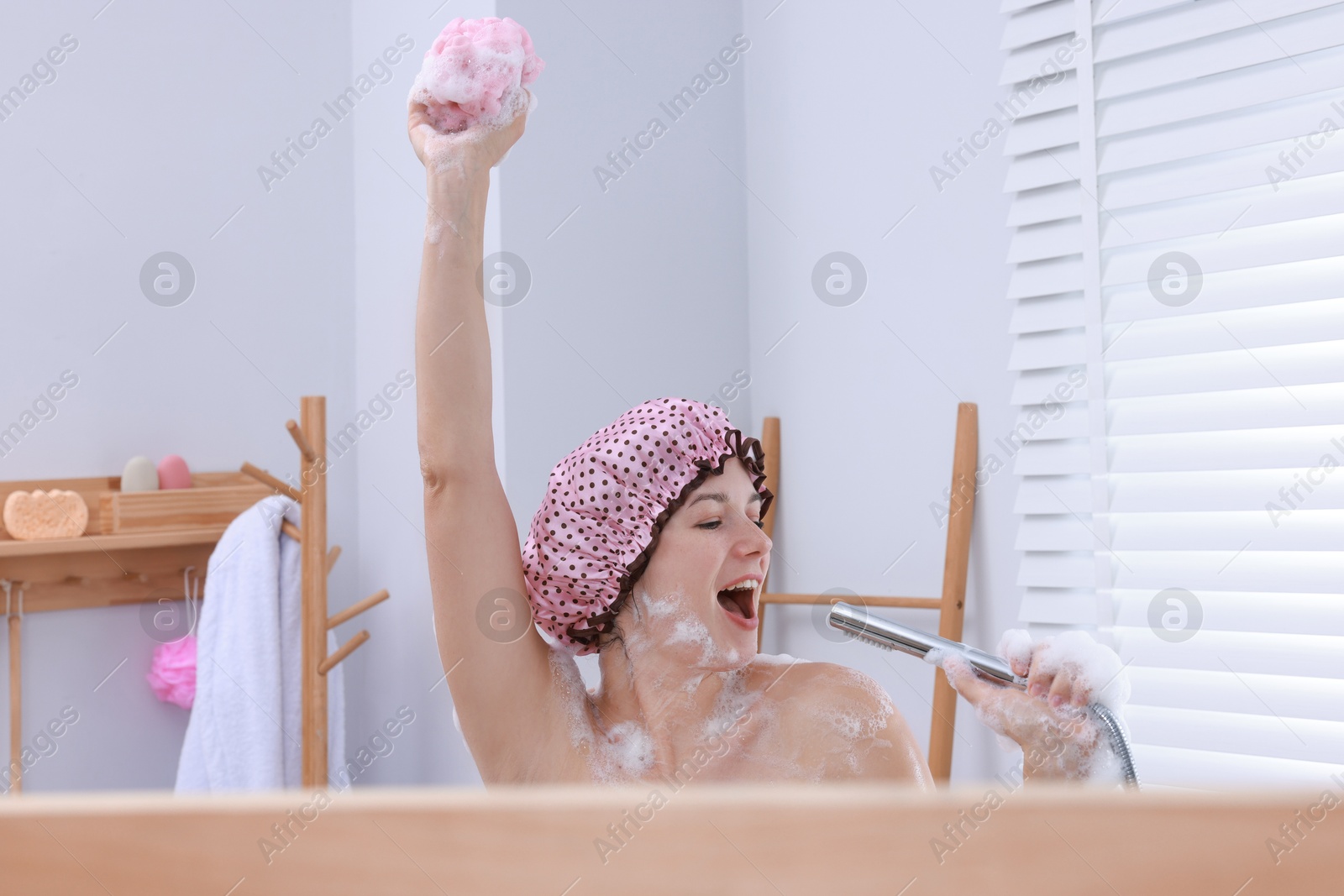 Photo of Woman with cap and mesh sponge singing while taking shower in bathroom