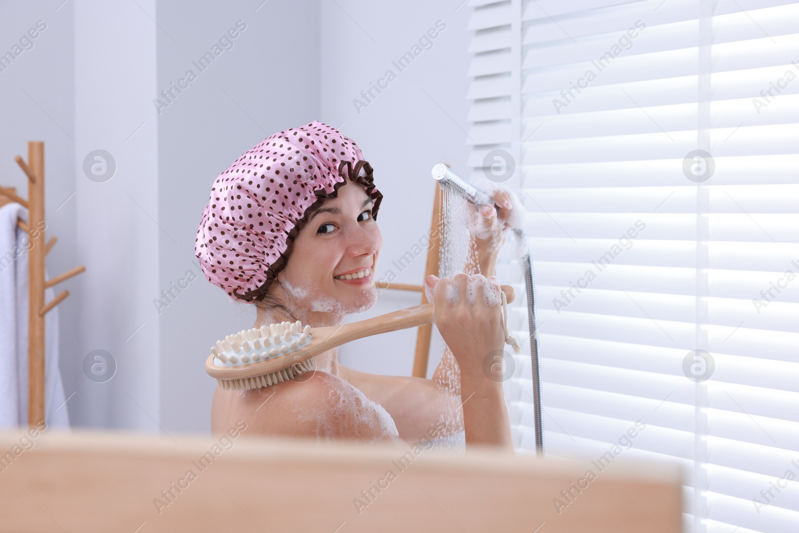 Photo of Woman with cap and brush taking shower in bathroom