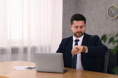 Photo of Banker checking time while working with laptop at wooden table in office. Space for text