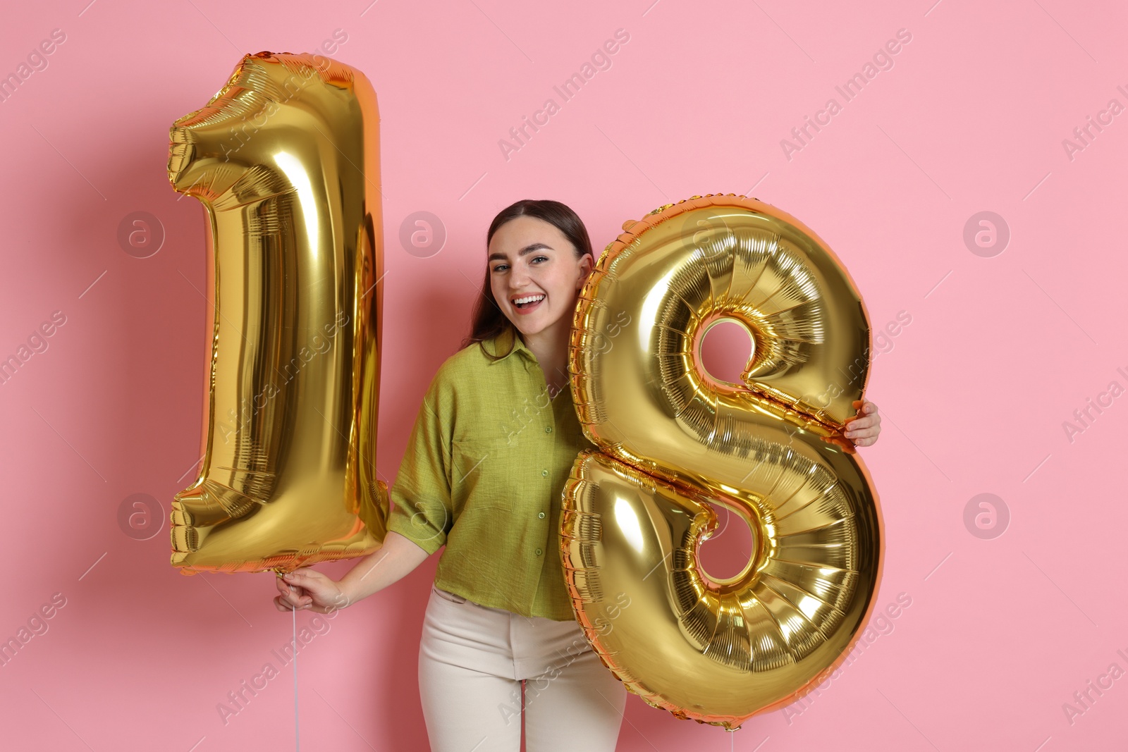 Photo of Coming of age party - 18th birthday. Happy young woman with number shaped balloons on pink background