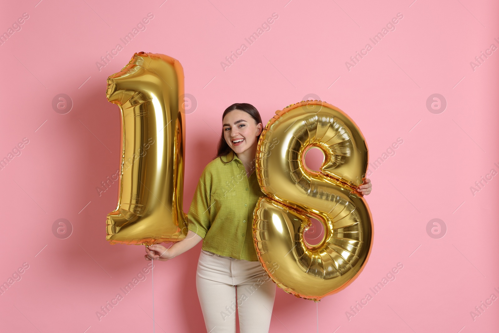 Photo of Coming of age party - 18th birthday. Happy young woman with number shaped balloons on pink background