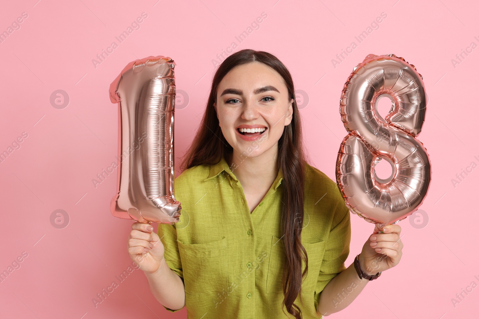 Photo of Coming of age party - 18th birthday. Happy young woman with number shaped balloons on pink background