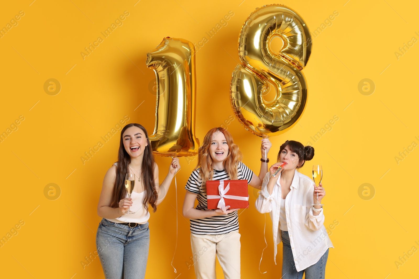 Photo of Coming of age party - 18th birthday. Group of young women celebrating with number shaped balloons on yellow background