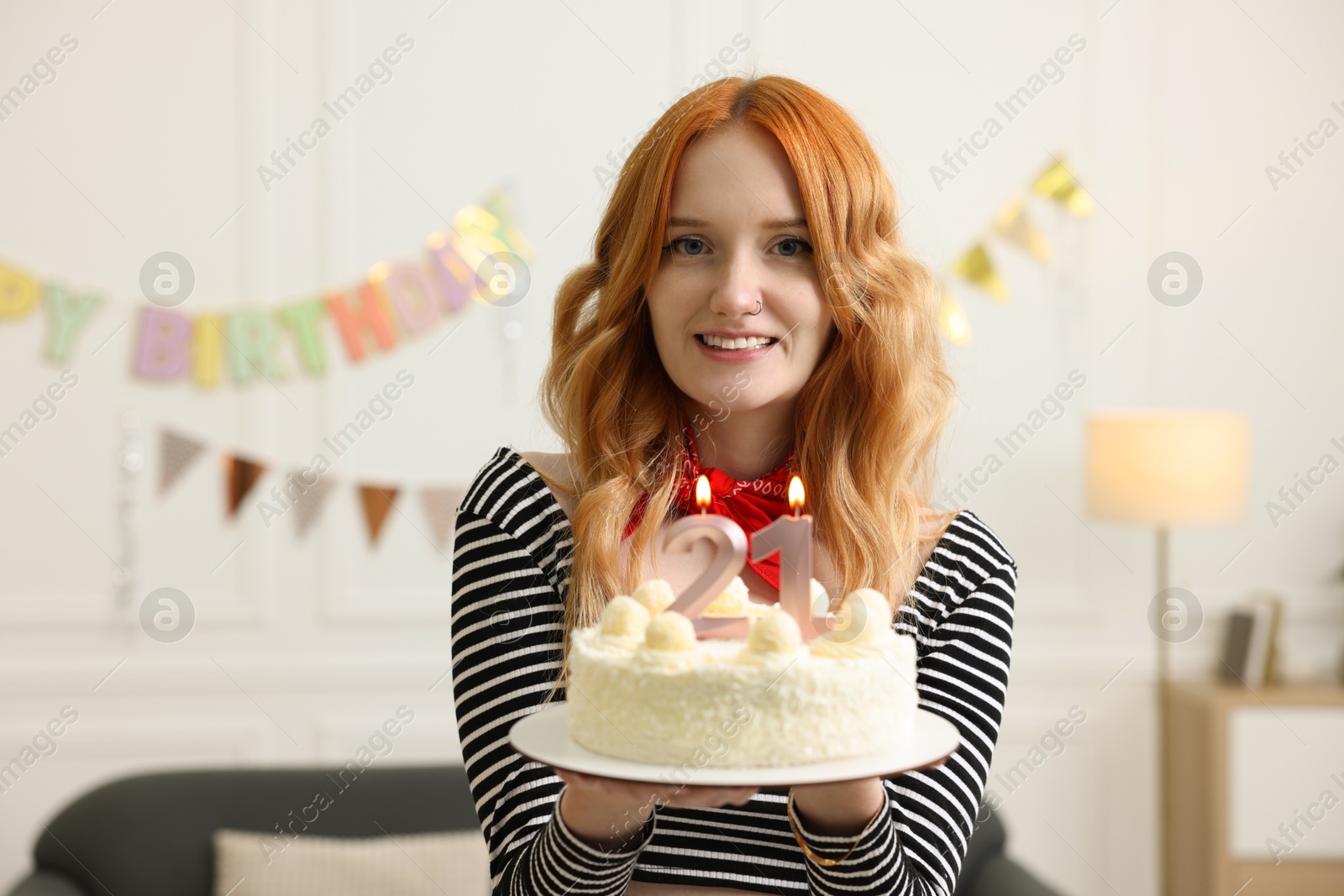 Photo of Coming of age party - 21st birthday. Happy young woman holding tasty cake with number shaped candles at home