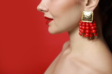 Photo of Beautiful young woman wearing elegant earrings on red background, closeup. Space for text