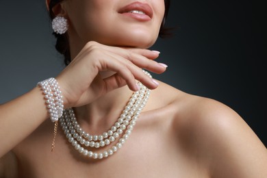 Photo of Woman wearing elegant pearl jewelry on dark grey background, closeup