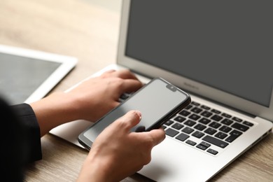 Photo of Businessman using laptop and smartphone at wooden table, closeup. Modern technology