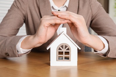 Photo of Property insurance. Real estate agent protecting house figure at wooden table indoors, closeup