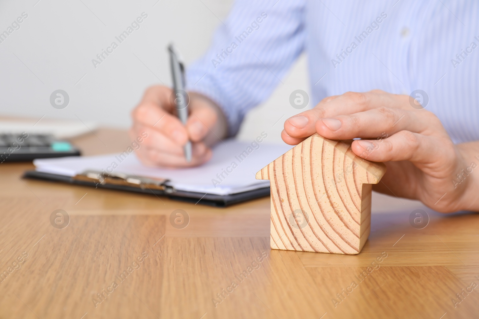 Photo of Property insurance. Real estate agent with house figure working at wooden table indoors, closeup